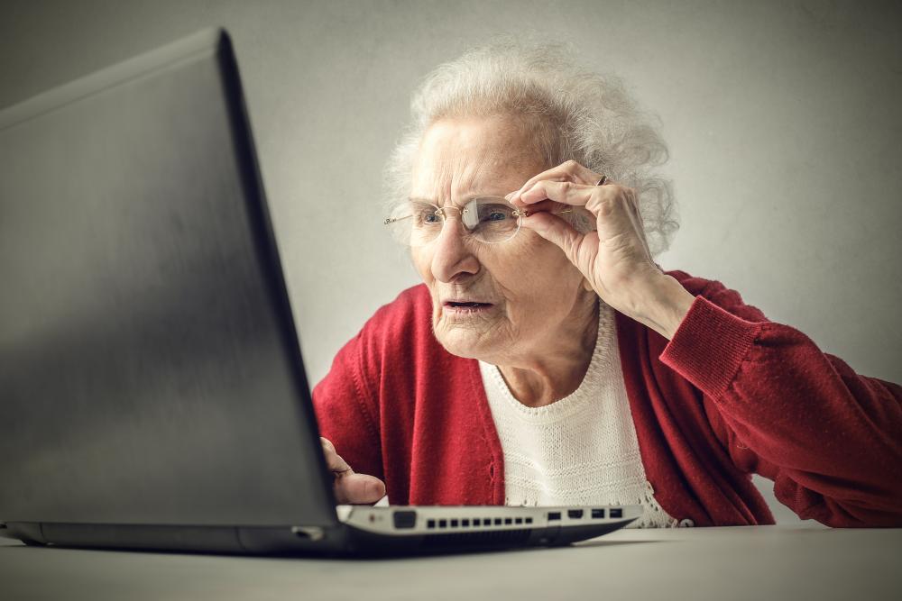 Iäkäs rouva lukee lasien kanssa tietokoneen ruudulta tekstiä